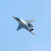 &quot;A modern single-engine combat fighter jet, similar to a light multirole aircraft, flying at high speed through a clear sky. The jet has a sleek aerodynamic fuselage, sharp nose, single air intake under the cockpit, and two large external fuel tanks on th icon
